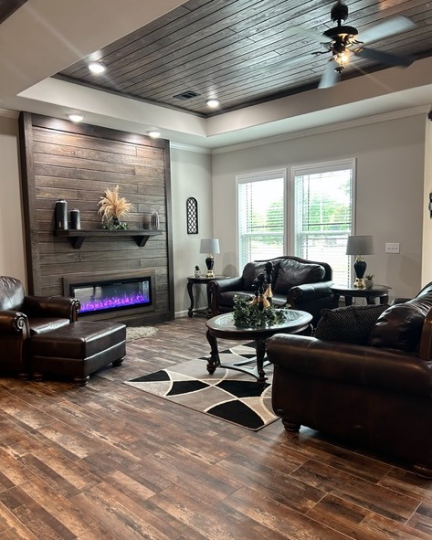 A cozy living room with brown leather sofas, a wooden floor, and a modern fireplace with purple flames. Soft lighting creates a warm, inviting atmosphere.