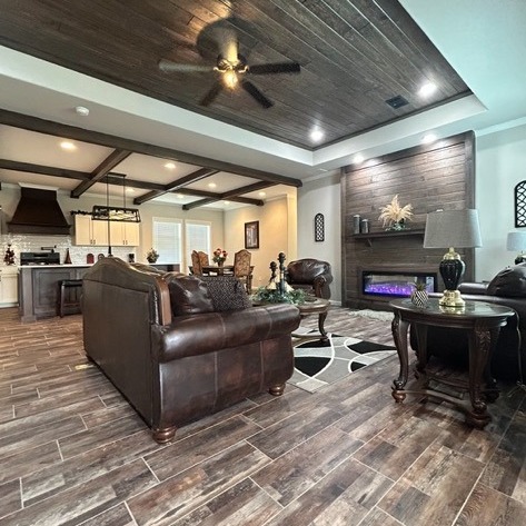 Spacious living room with rich leather sofas, a modern kitchen in the background, wooden ceiling accents, and a cozy fireplace with a warm, elegant ambiance.