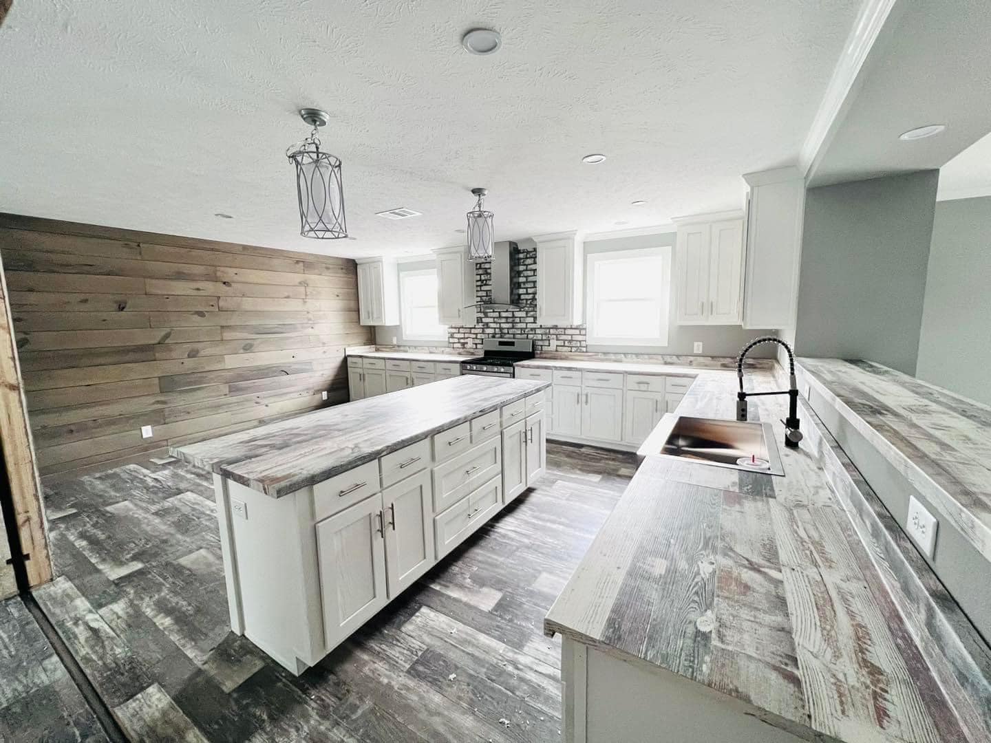 Spacious kitchen with rustic wood floors, white cabinets, and brick backsplash. Features two islands, pendant lights, and large windows. Bright and inviting.