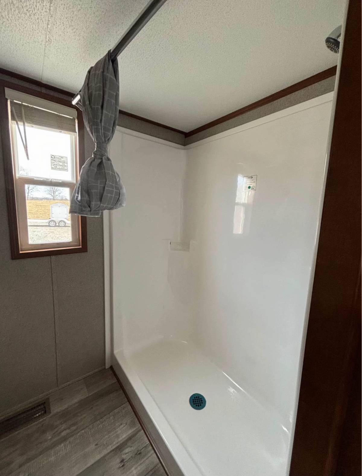 Simple bathroom with a white shower, gray curtain partially drawn on a rod, and a window letting in natural light. The room has a calm, minimalistic feel.