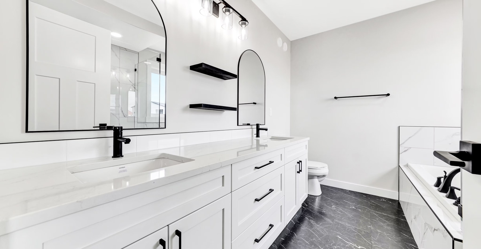 A modern bathroom with a sleek white double vanity, black fixtures, arched mirrors, and black marble floor. The tone is minimalist and elegant.
