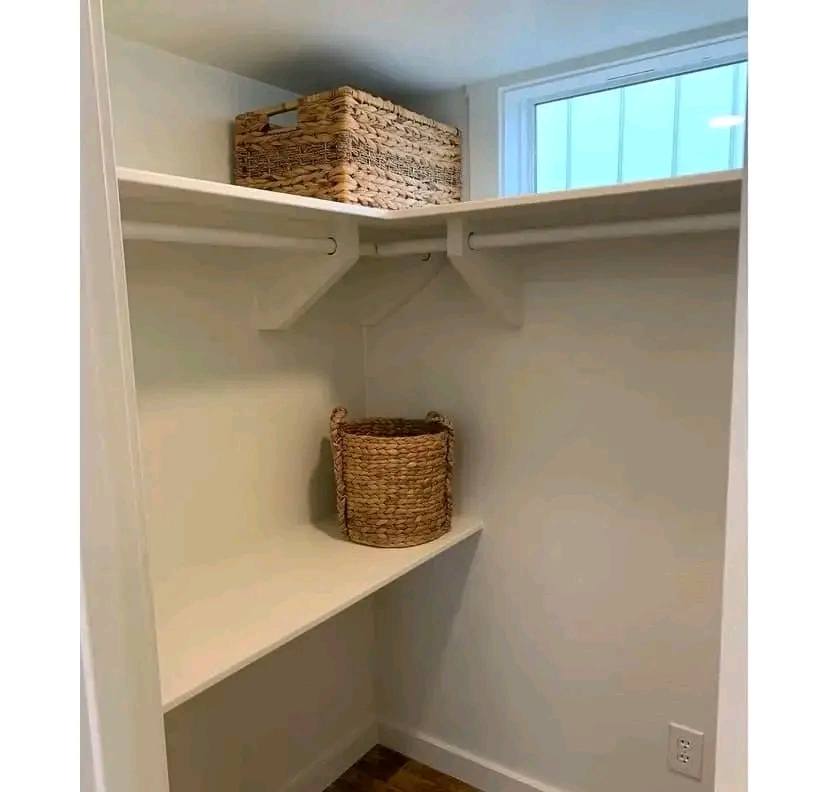 Empty white closet with two woven baskets; one rectangular on a shelf, another round below. A window brings in natural light, creating a minimalistic feel.