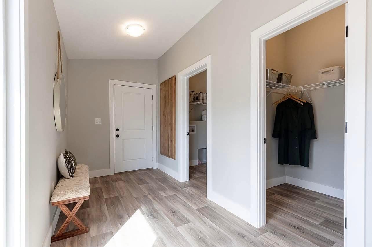 Bright hallway featuring light wood floors, a cushioned bench, and two open closets. Neutral tones convey a clean, organized feel.