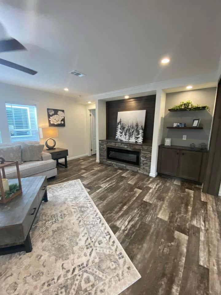 A cozy living room with a stone fireplace, modern art, and wooden floors. A grey sofa and coffee table add warmth. Soft lighting and decor create an inviting atmosphere.