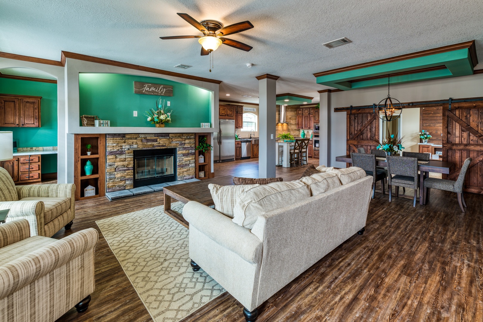 Spacious living room with a beige sofa, brick fireplace, and hardwood floors. Open layout to the kitchen, dining area with rustic barn doors. Cozy and inviting.