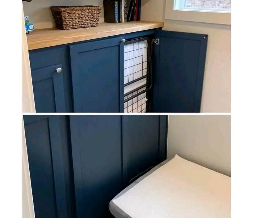 Blue cabinet with wooden top reveals a fold-out bed. The interior holds books and a wicker basket. The setting is practical and modern.