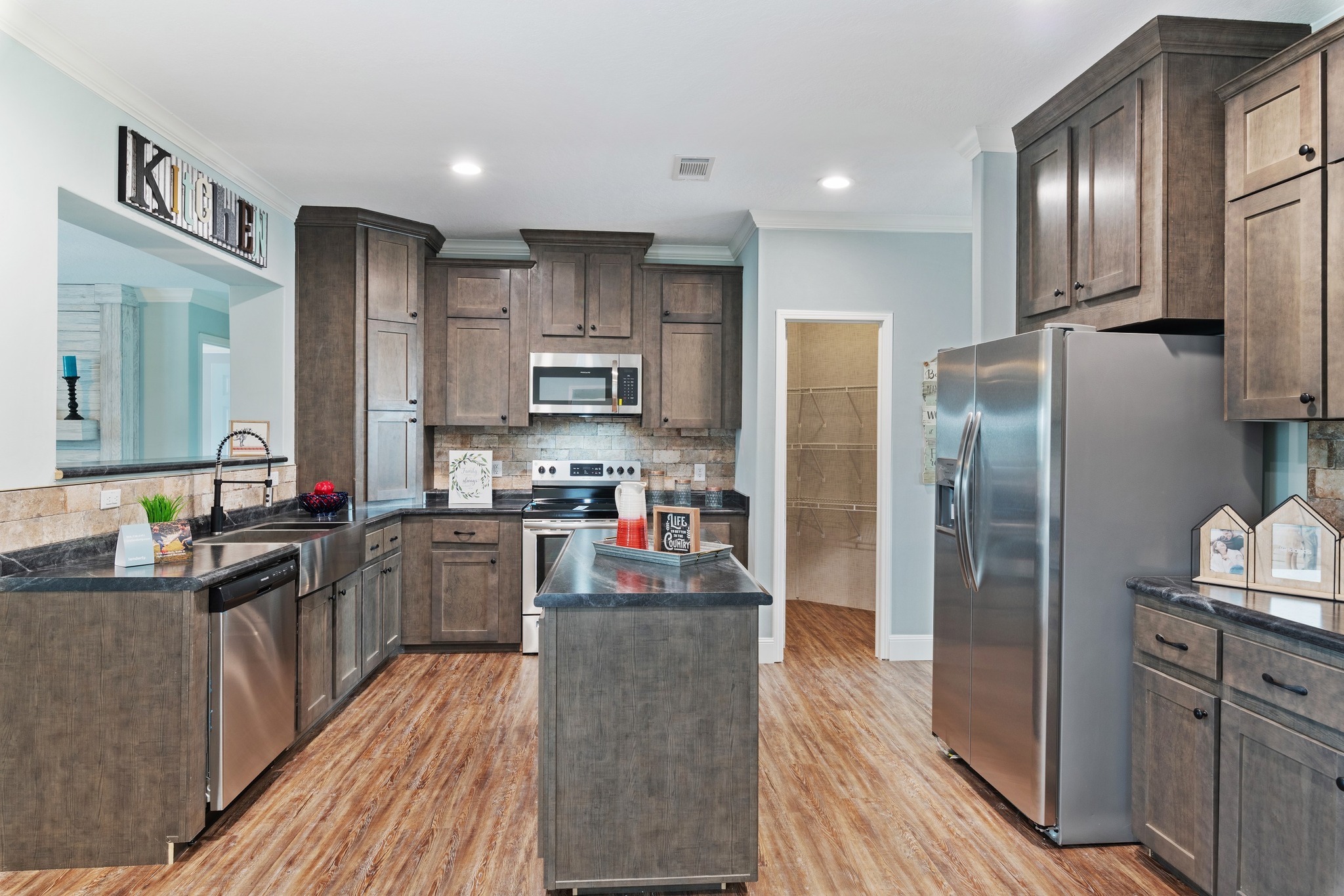 Spacious kitchen with dark wood cabinets, stainless steel appliances, and a central island. Light wood floor adds warmth, creating a cozy atmosphere.