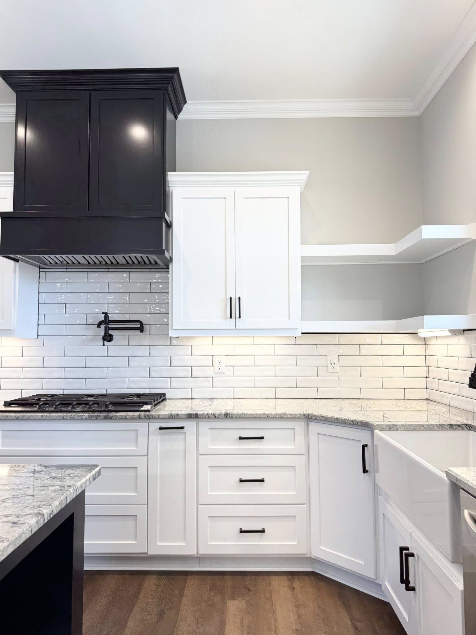 A modern kitchen with sleek design elements features a black island and cabinets, white backsplash, pendant lighting, hardwood floors, and stainless steel appliances.
