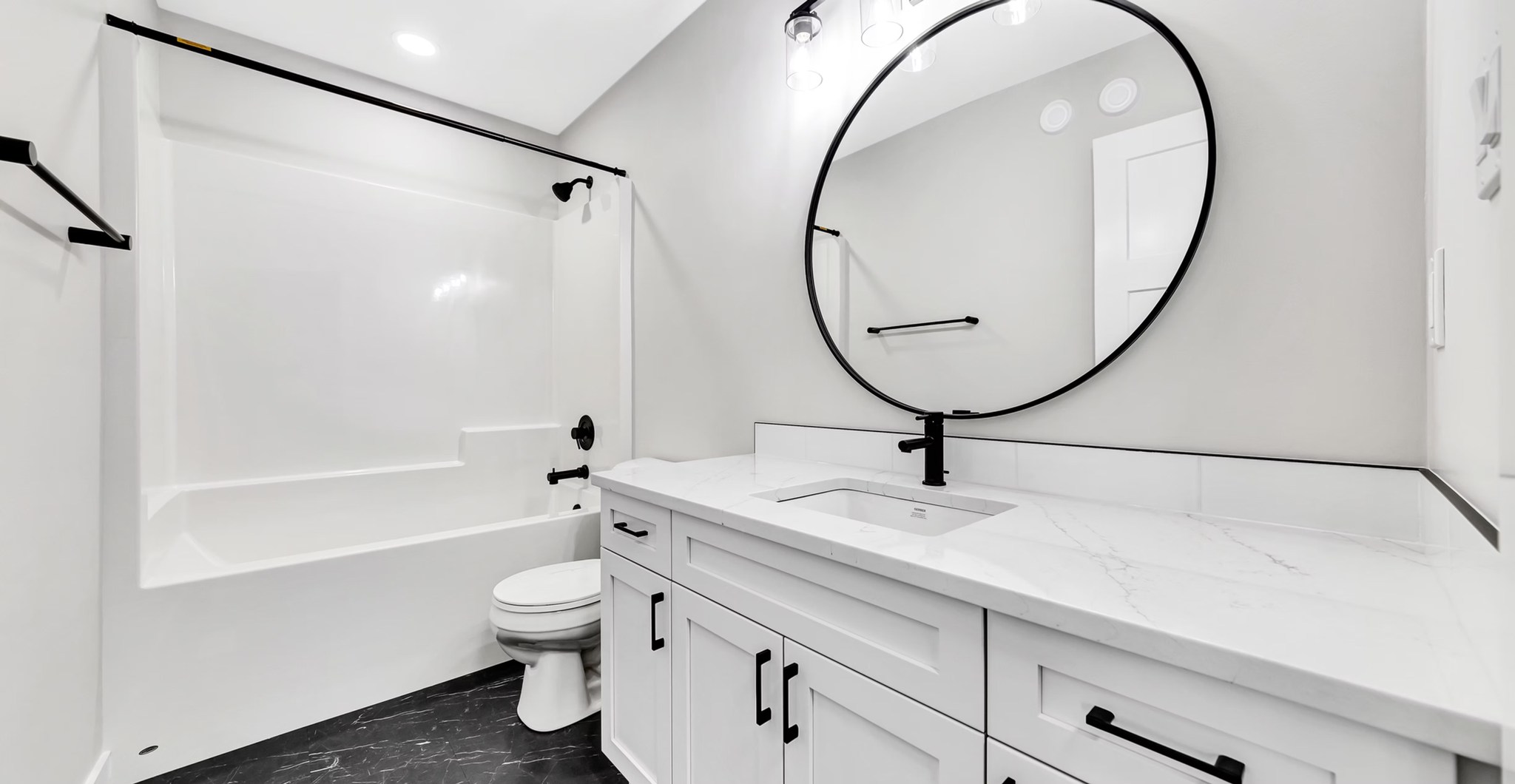 Modern bathroom with sleek design. Features white vanity with black fixtures, large round mirror, and bathtub. Clean, minimalist, and sophisticated ambiance.