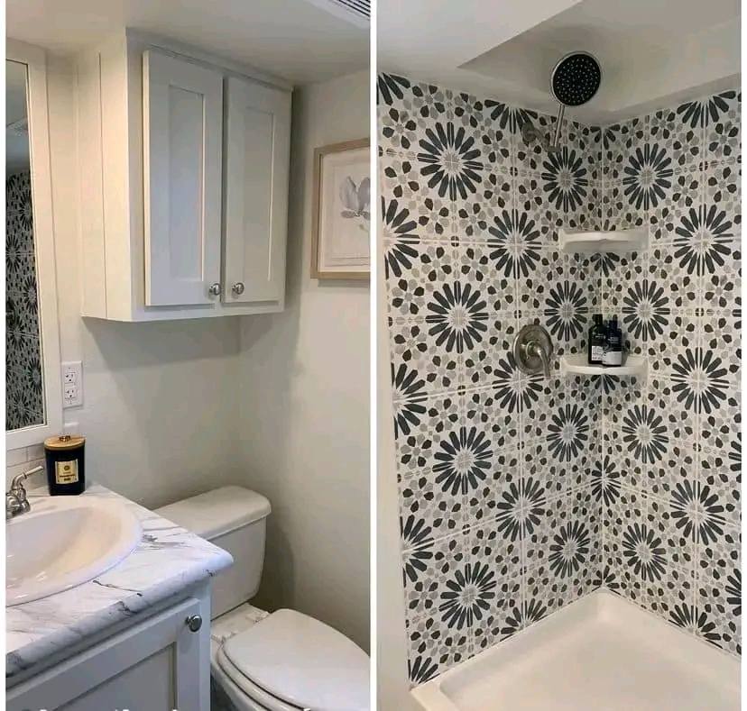Cozy bathroom with a marble sink, white cabinet, and toilet on the left; shower with floral-patterned tiles and corner shelves on the right. Clean and modern.