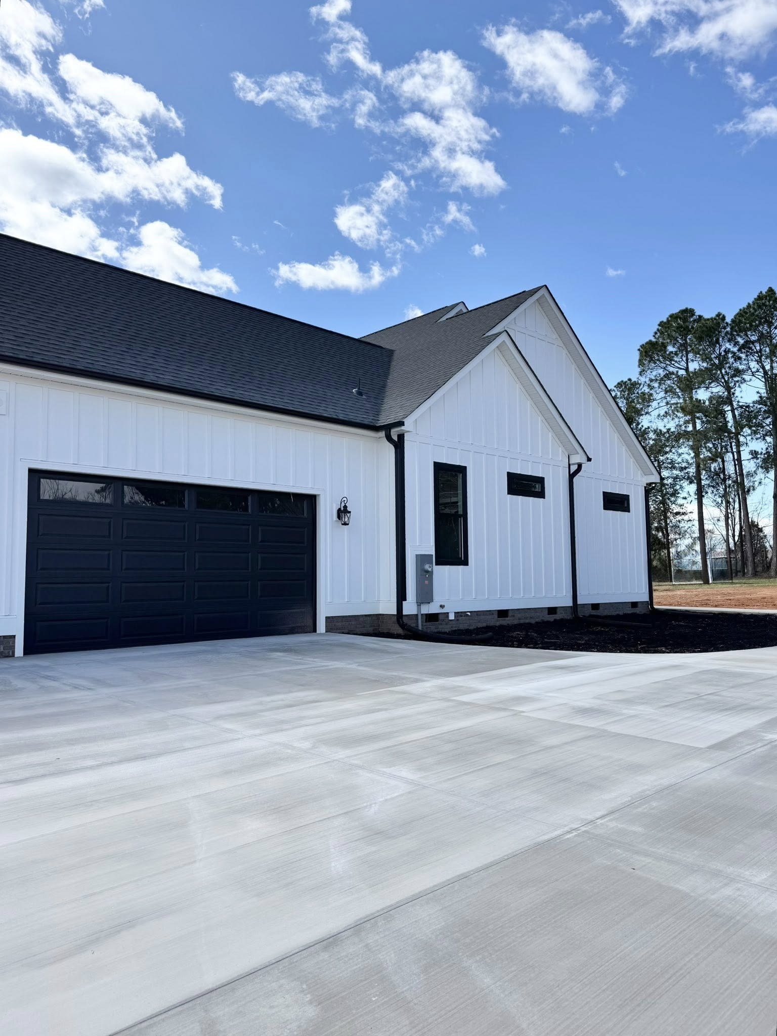 A modern white house with black trim, featuring a large black garage door. The sky is blue with fluffy clouds, evoking a crisp, clear day.
