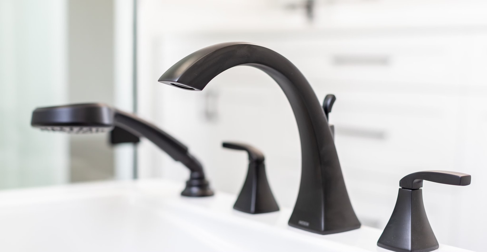 Close-up of a modern black faucet and handles on a white bathtub, with a sleek showerhead in the background. The scene is clean, minimalist, and elegant.