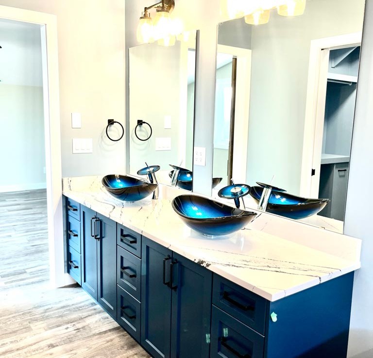 Modern bathroom vanity with blue cabinets, marble countertop, and two blue glass vessel sinks. Large mirrors and bright lighting create a sleek, elegant look.