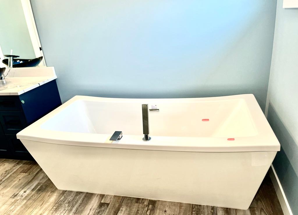 A modern bathroom with a white, rectangular bathtub against a pale blue wall. The bathtub has sleek metal fixtures, adjacent to a dark vanity.