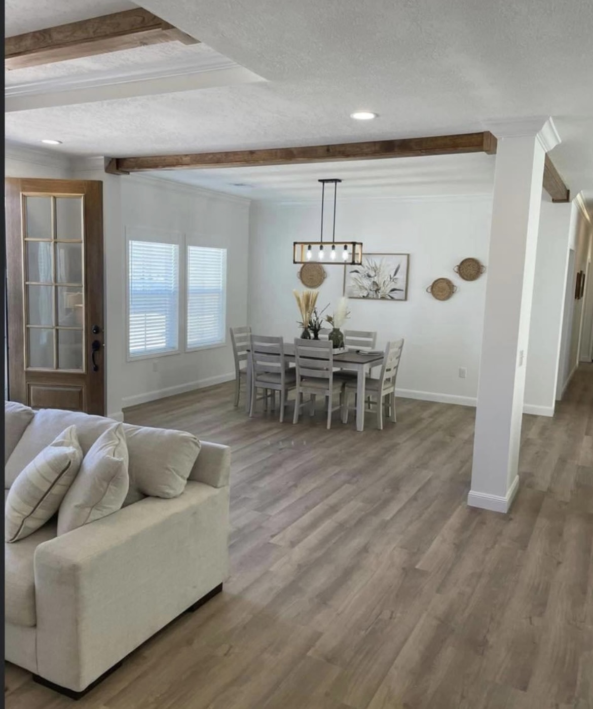 Modern dining area with a cozy vibe features a wooden table and six chairs. Natural light shines through windows, highlighting wooden beams and decor.
