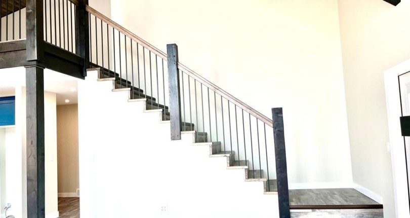 Modern interior featuring a black-railed staircase with wooden steps, contrasting against white walls and a high ceiling, creating an airy, open feel.