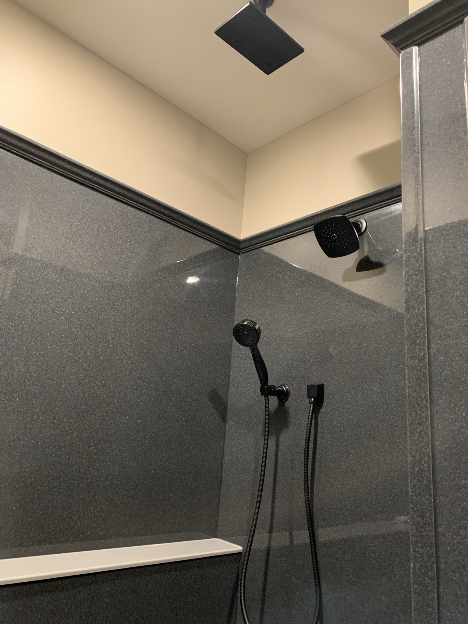 Modern shower with dark gray walls featuring a sleek rainfall showerhead and handheld sprayer. The design is minimalist and elegant.