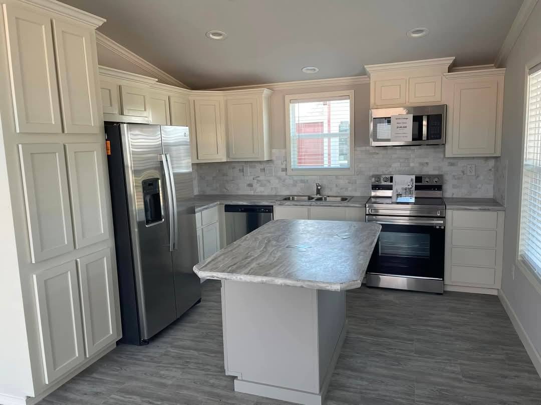 Bright kitchen with white cabinets, marble island, and stainless appliances. A large window and light gray wood flooring create an inviting atmosphere.