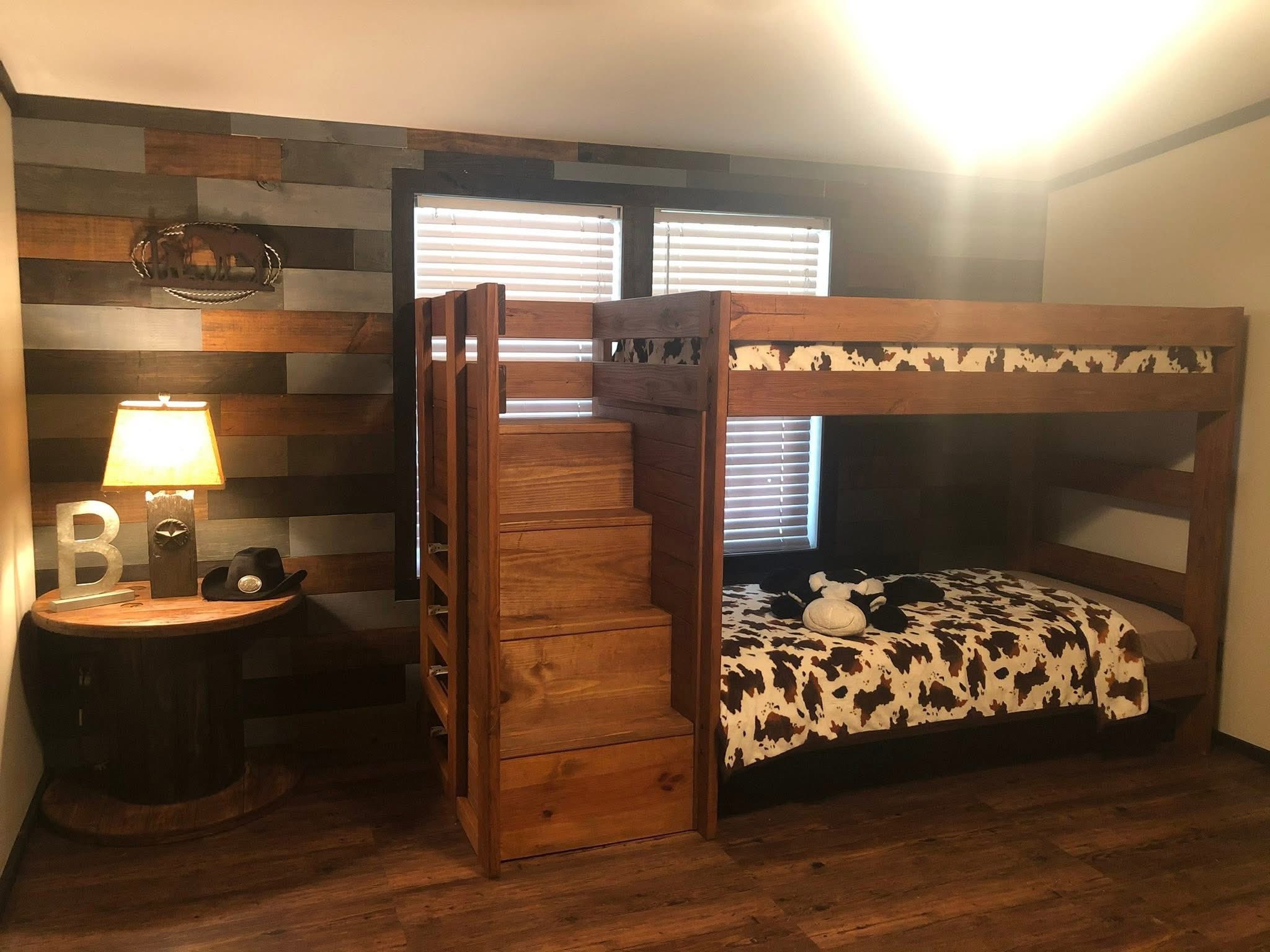 Cozy room with a wooden bunk bed featuring cow-print bedding, beside a lamp on a rustic table. The wooden accent wall adds a warm, rustic feel.