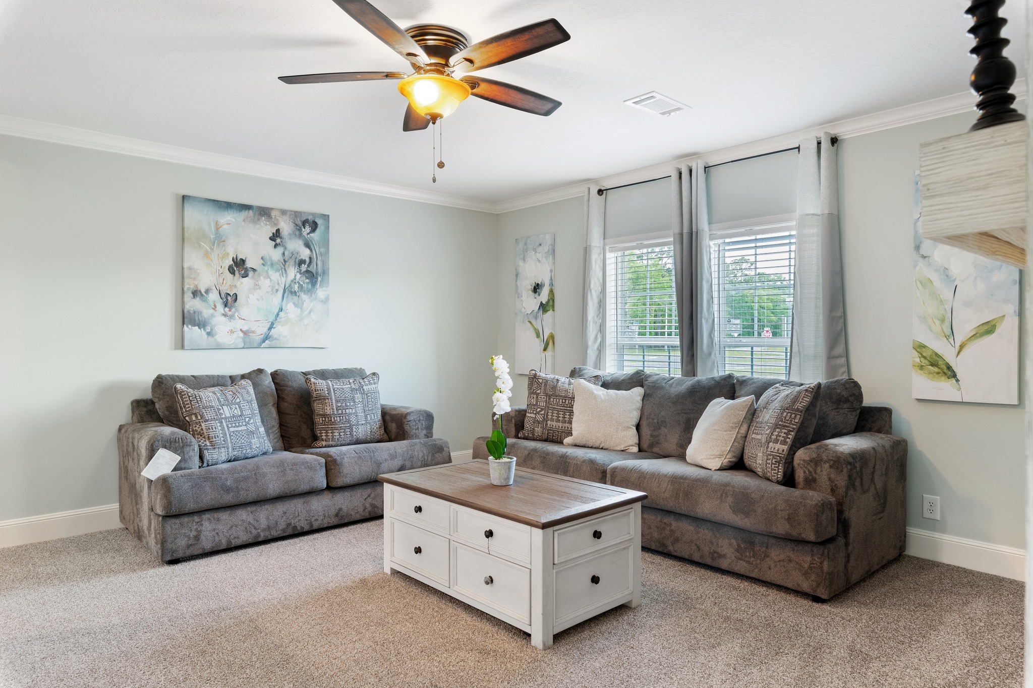 A cozy living room with two grey sofas, floral paintings, and a wooden coffee table. A modern fireplace is set in a shiplap-paneled wall, exuding warmth.