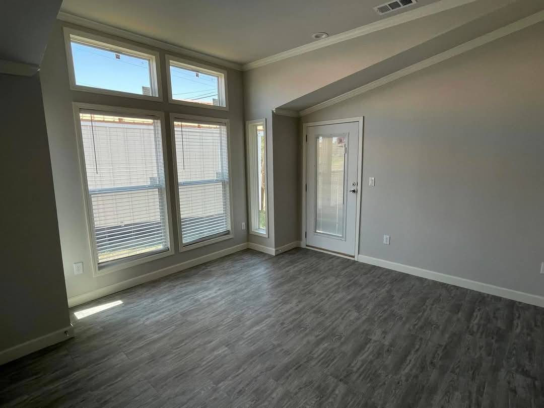 Empty room with large windows and a glass door, allowing abundant natural light. The space has gray flooring and neutral-colored walls, creating a calm ambiance.
