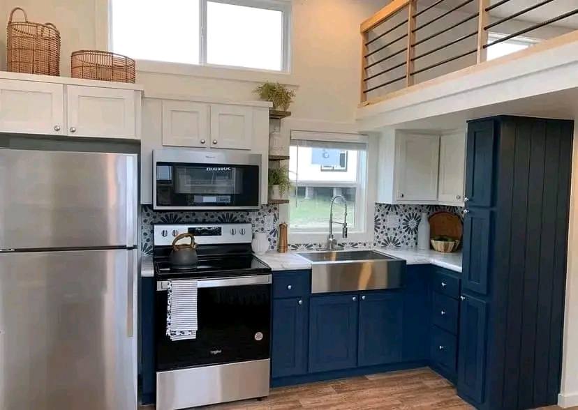 Modern kitchen with navy and white cabinets, stainless steel appliances, and a farmhouse sink. Decor includes wicker baskets and plants, exuding a cozy vibe.
