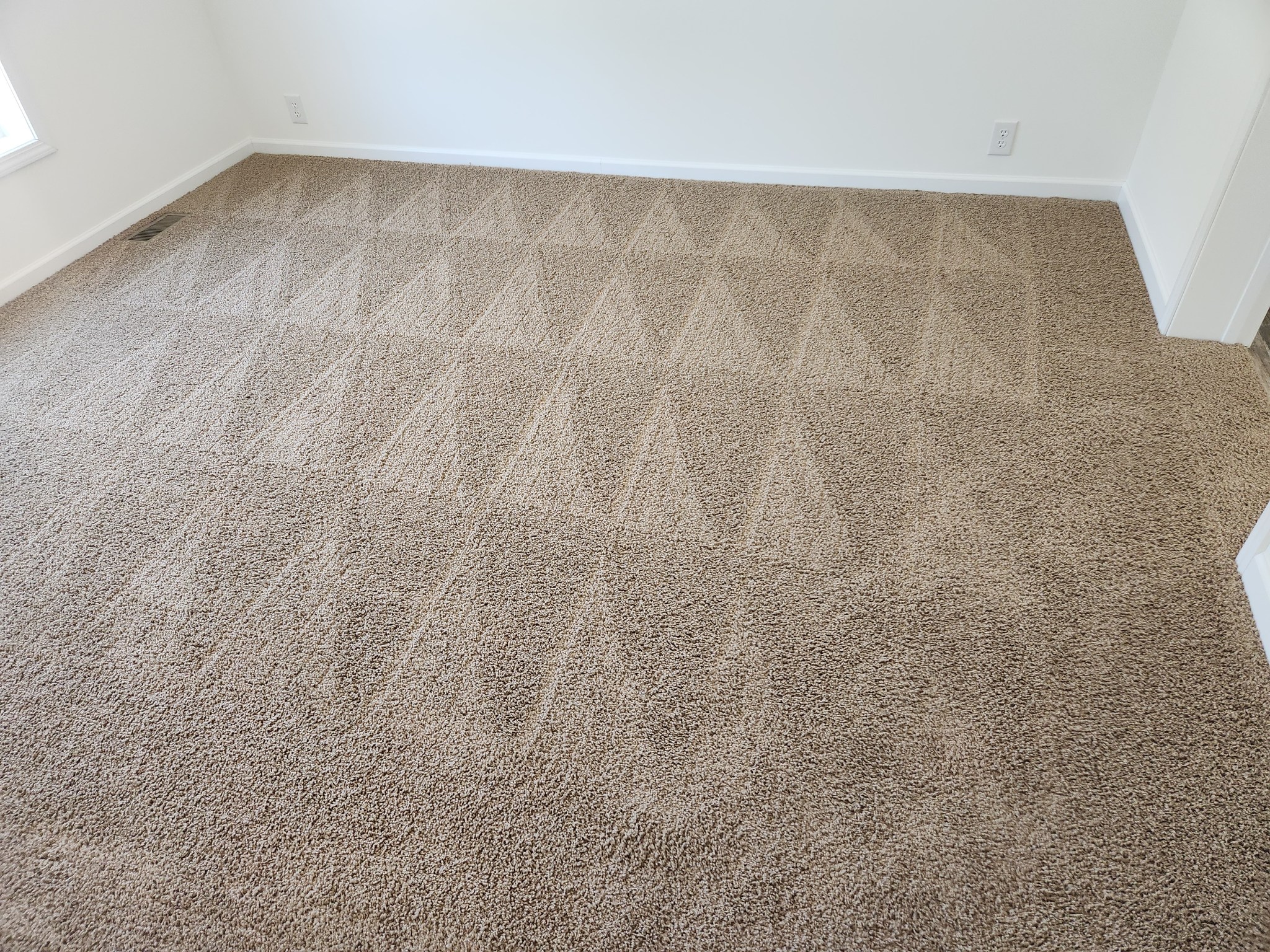 Beige carpet with a repeating pattern of light geometric triangles, creating a sense of order and symmetry in a bright, empty room.