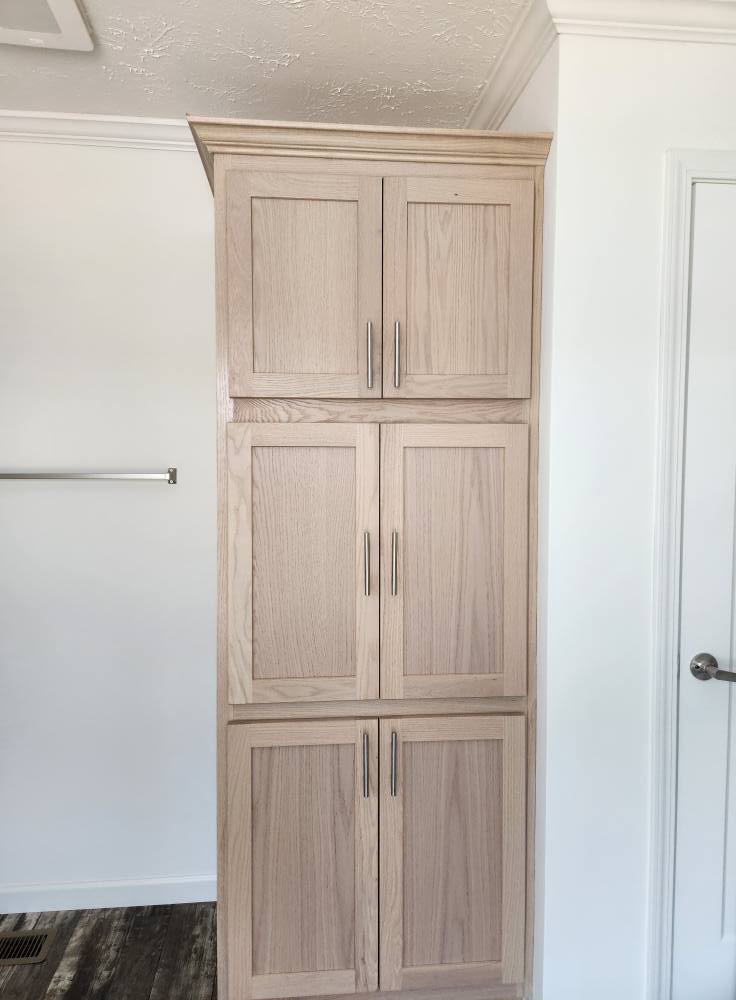 Light wood cabinet with six panels and metal handles against a white wall. The room has a modern and clean look, with light hardwood floors.
