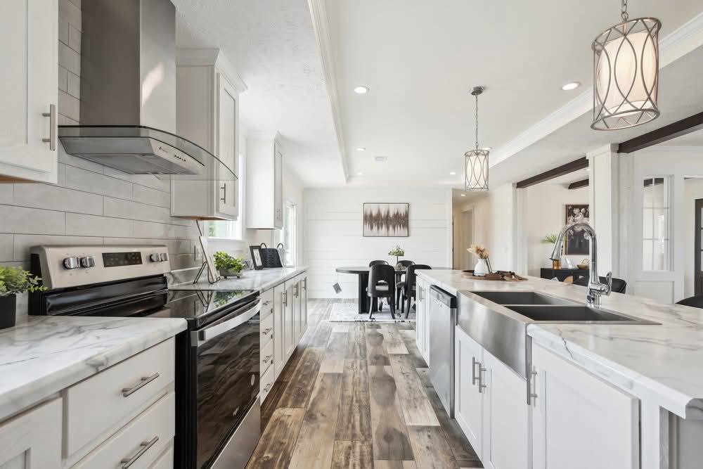 Modern kitchen with marble countertops, stainless steel appliances, and wooden floors. Bright lighting from hanging fixtures creates a cozy ambiance.