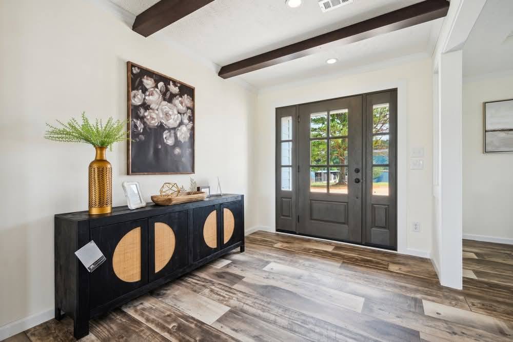 Stylish entryway with light wood flooring, a black console with decorative patterns, a vibrant plant in a gold vase, and a modern floral painting.