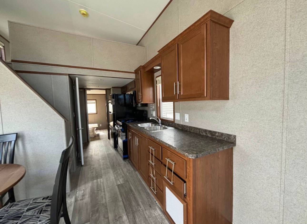 Compact kitchen in a narrow mobile home with wood cabinets, dark countertops, a stainless steel sink, and a black stove. Modern and tidy ambiance.