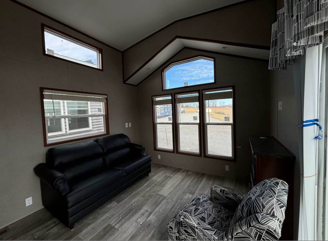Interior of a cozy room with large windows, a patterned armchair, and a small fireplace. Bright, natural light and outdoor view create a serene atmosphere.
