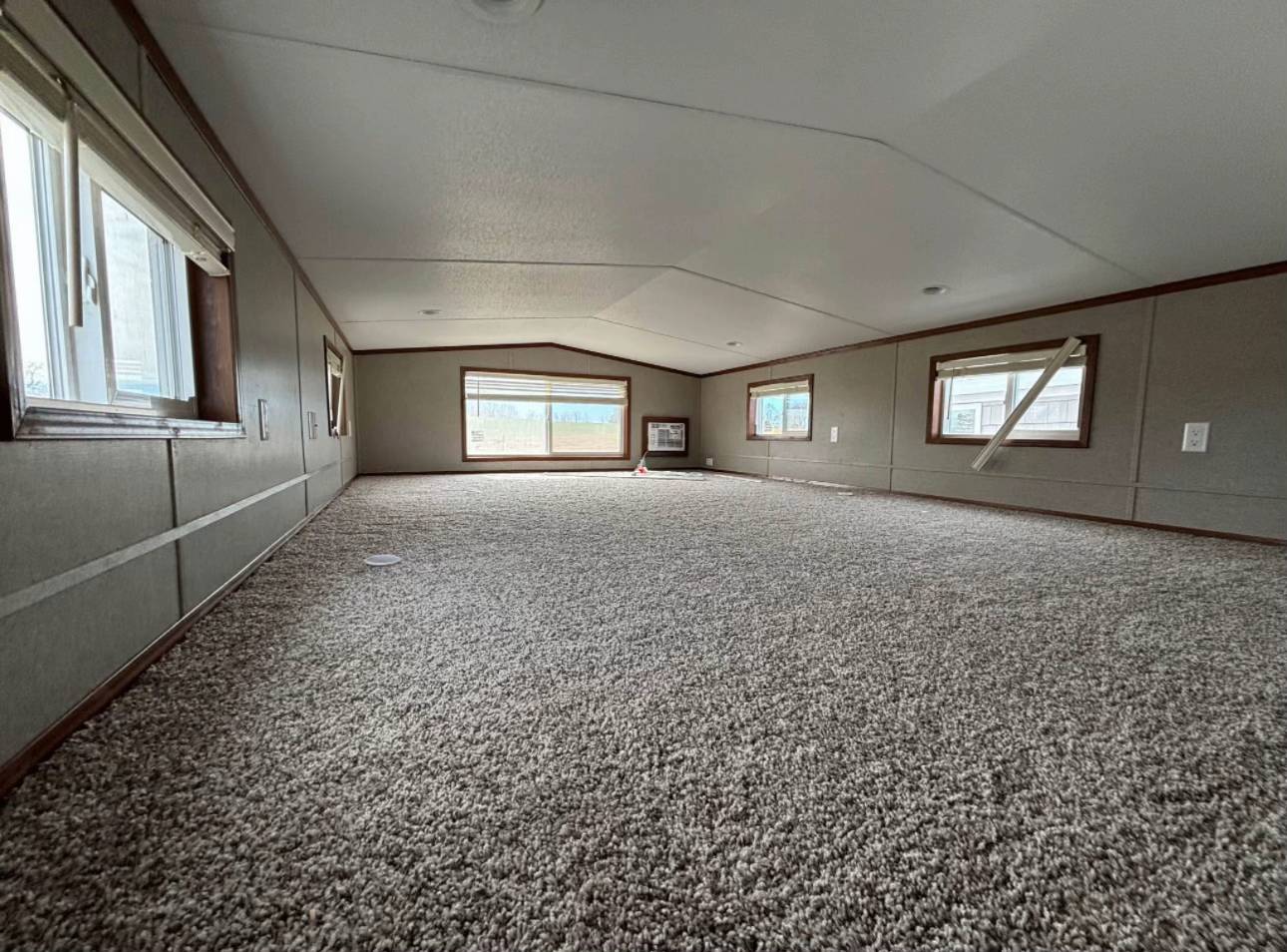 Spacious carpeted attic room with angled ceiling, large windows, and soft natural light. Cozy, inviting space with a tranquil, serene ambiance.