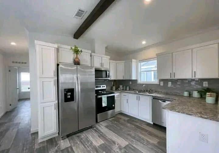 Modern kitchen with white cabinets, stainless steel appliances, and a granite countertop. Light gray wood flooring and a small window create a bright, clean ambiance.