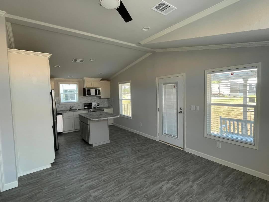 Bright, modern kitchen and living area with gray laminate flooring. White cabinets, stainless steel appliances, and French doors enhance the spacious feel.