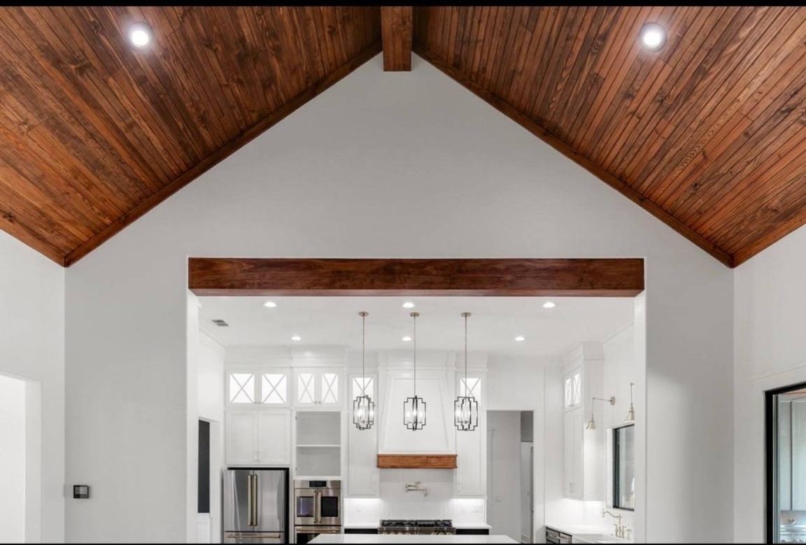 Spacious kitchen with high vaulted wooden ceiling, white walls, and modern lighting. Stainless steel appliances and sleek cabinets create a clean, inviting ambiance.