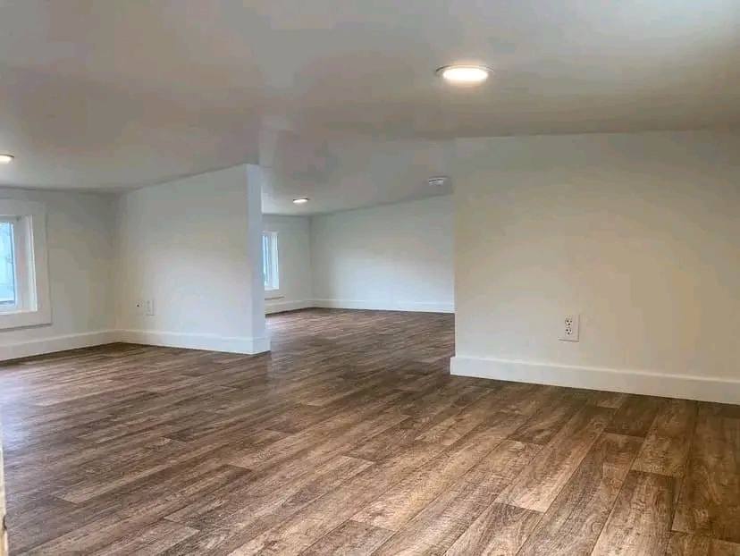Spacious room with white walls, wooden flooring, and two small windows. Ceiling lights illuminate the minimalistic, serene atmosphere.