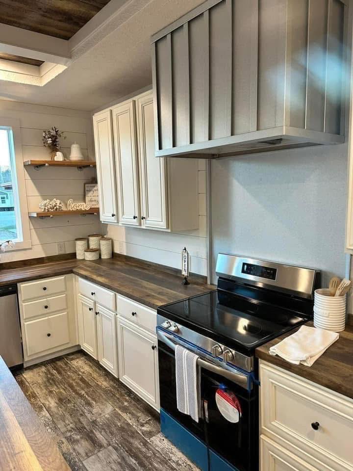 Modern kitchen with white cabinets, dark wood countertops, and stainless steel appliances. Open shelves display decor, creating a cozy, organized atmosphere.