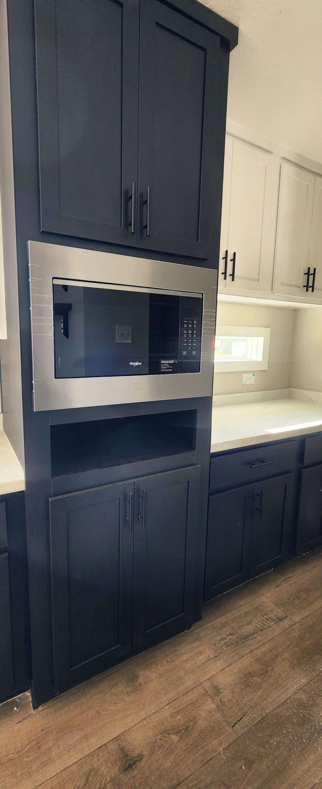 Tall, modern kitchen cabinets in dark wood feature a built-in stainless steel microwave. Light countertops and hardwood floors add contrast and warmth.