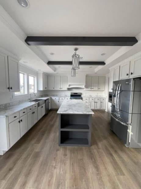 Spacious kitchen with white cabinets, marble island, stainless steel appliances, and wood flooring. Bright and modern with a cozy, welcoming feel.