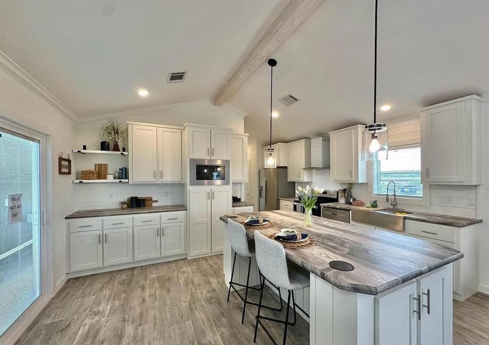 Spacious modern kitchen with white cabinets, wood flooring, and a large island with bar stools. Pendant lights hang above, creating a warm ambiance.