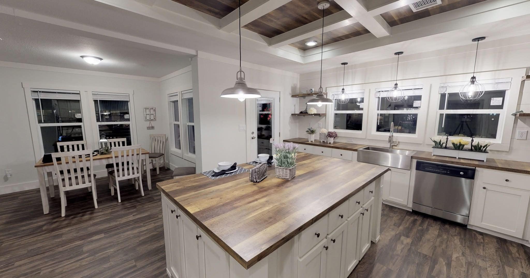Modern kitchen with white cabinets, wood countertops, and pendant lights. Large island in center. Dining area with white table and chairs. Cozy and inviting atmosphere.