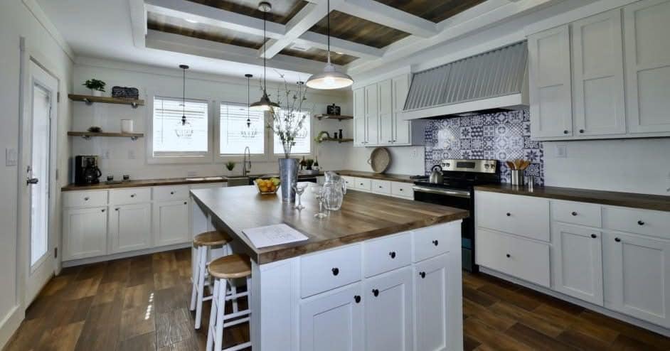 Spacious kitchen with white cabinets, wooden countertops, and a large island with stools. Pendant lights hang above. The atmosphere is modern and cozy.