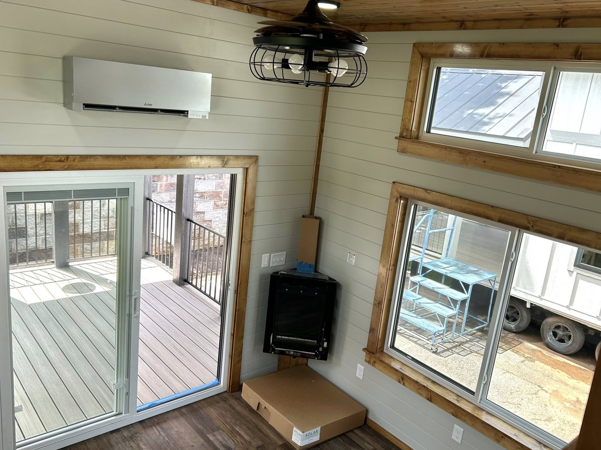 View of a cozy, well-lit room with shiplap walls, wood trim, air conditioner, and sliding glass doors leading to a deck. Modern light fixture above.