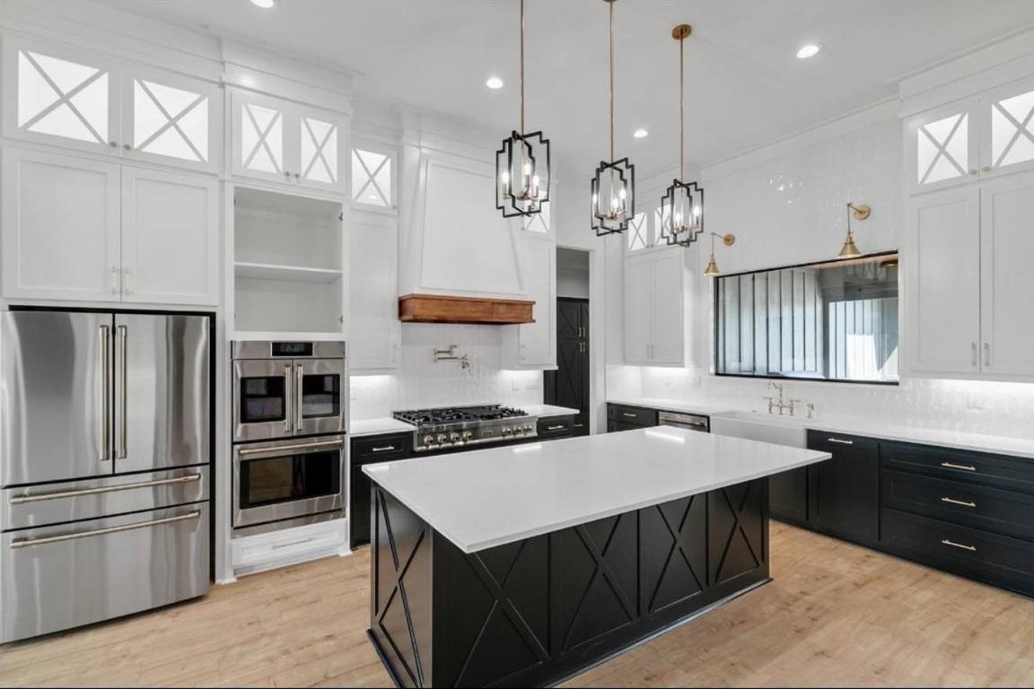 Spacious modern kitchen with a large black and white island under three geometric pendant lights. Stainless steel appliances and elegant cabinetry accent the space.