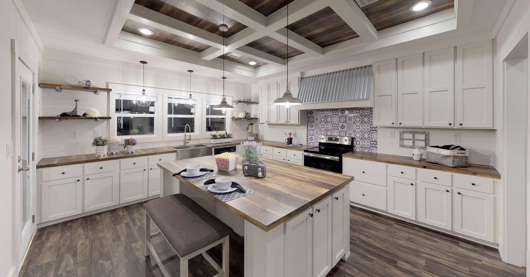 Spacious kitchen with white cabinets, wooden countertops, and a central island. Pendant lights hang from a beamed ceiling. Cozy and elegant.