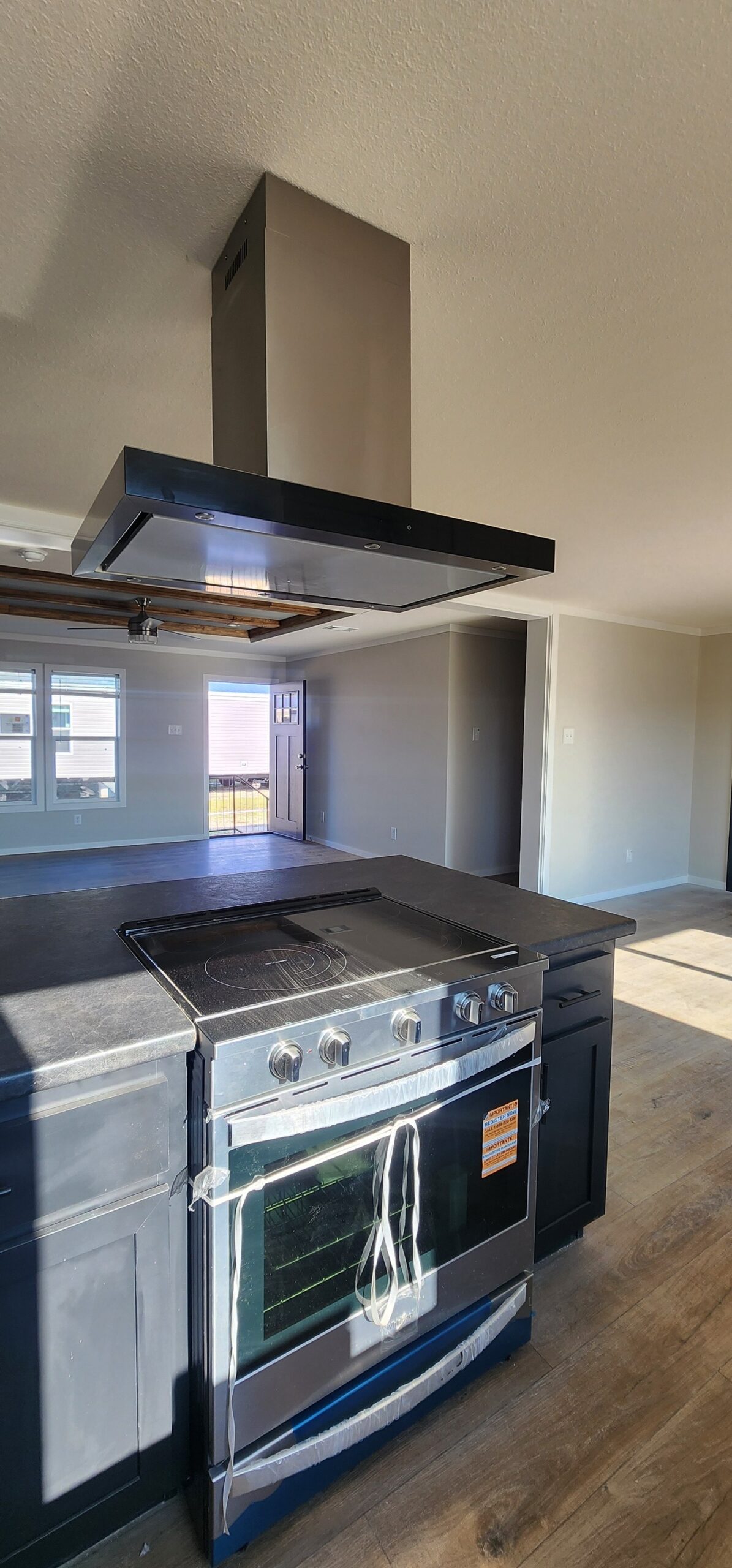 Modern kitchen interior with a sleek stainless steel stove and overhead range hood on a dark countertop. Bright sunlight floods through large windows, enhancing the airy ambiance.