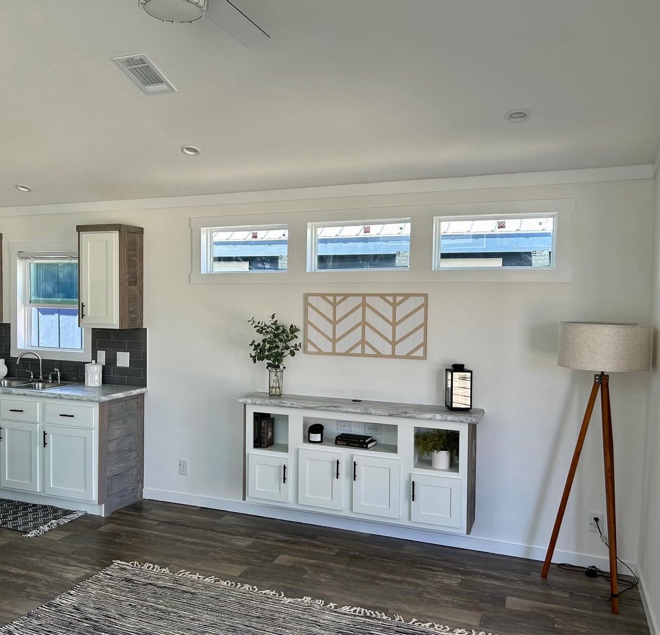 Bright, modern kitchen with white cabinets, gray backsplash, and a small indoor plant. The cozy room features a warm wooden floor and ambient lighting.