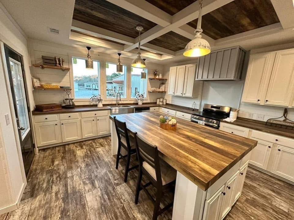 Rustic kitchen with white cabinets, large wooden island with chairs, and dark wooden floors. Warm lighting and a cozy ambiance with natural accents.
