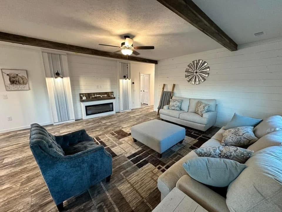 Stylish living room with modern furniture, neutral tones, and rustic accents. Features a cozy fireplace, ceiling fan, and decorative wall items.